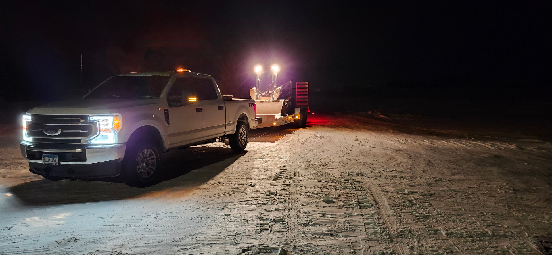 Night snow crew with skid steer on trailer